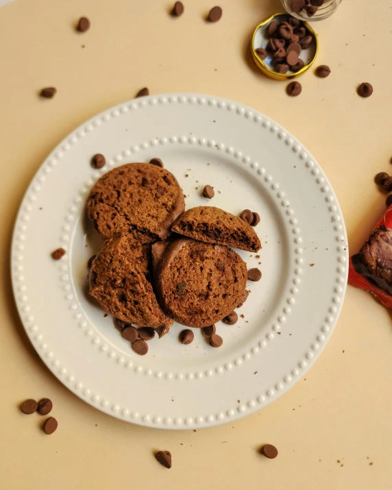 two chocolate chip cookies on a plate next to half filled chocolate chips