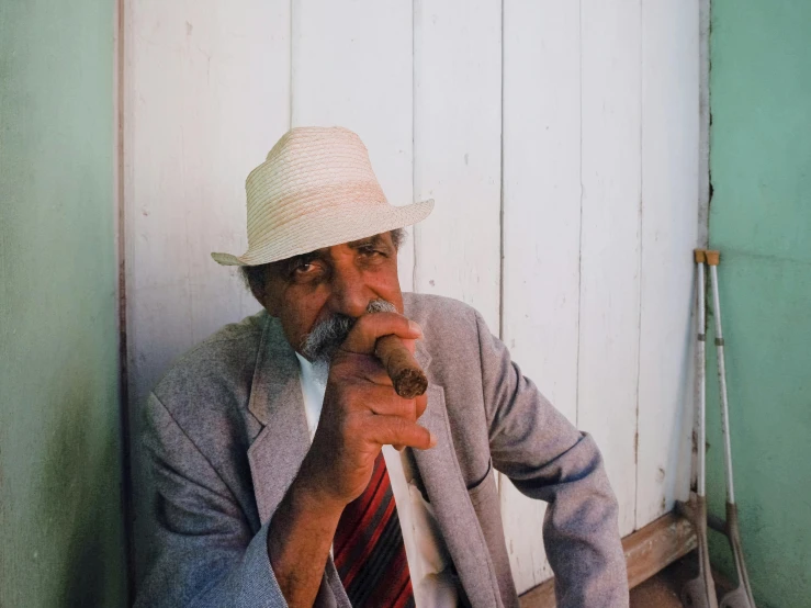 a man sitting and smoking while wearing a suit and hat