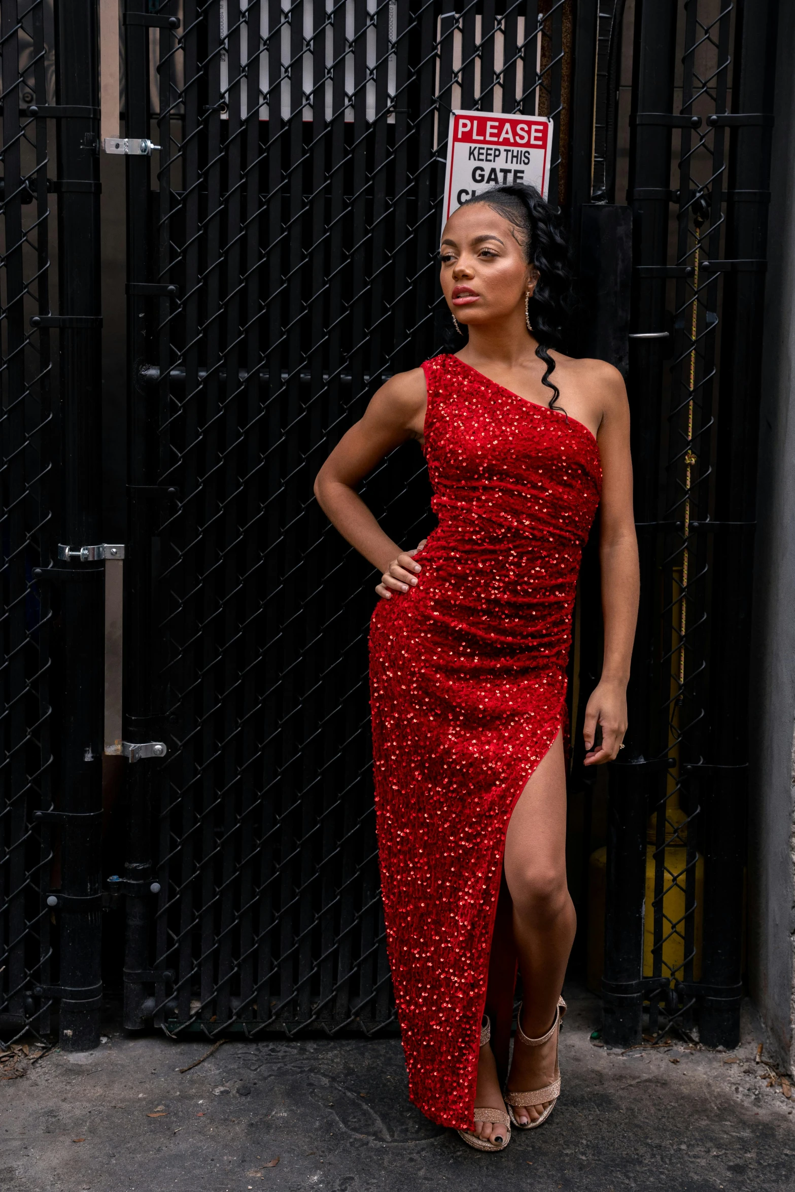 a woman standing next to a fence wearing a red dress