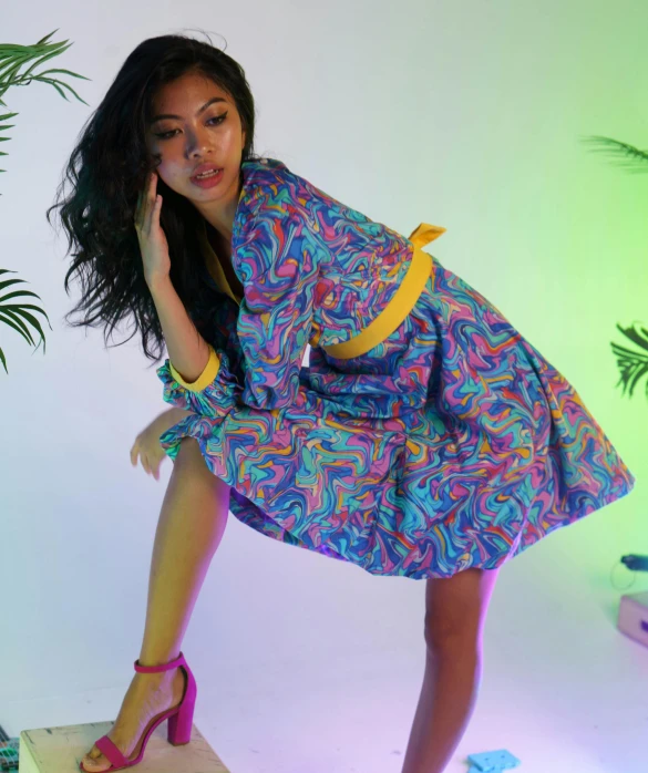 young woman with her foot up on a block, posing in a brightly colored dress