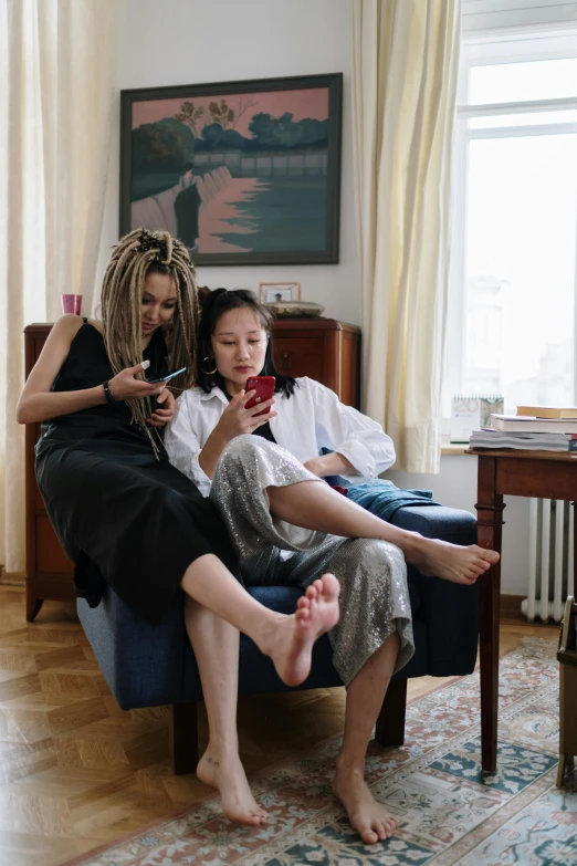 two women sitting on a chair holding a smart phone