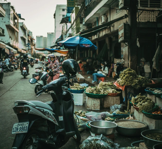 the motor bike is parked in front of the vegetable vendor