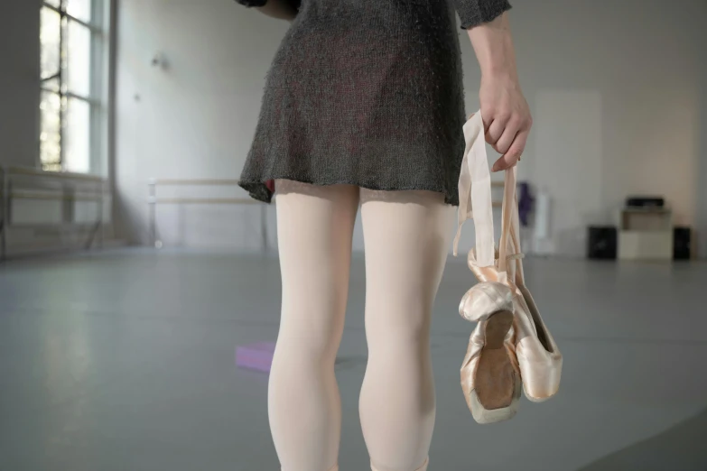 woman in tights and ballet shoes holding ballet shoe