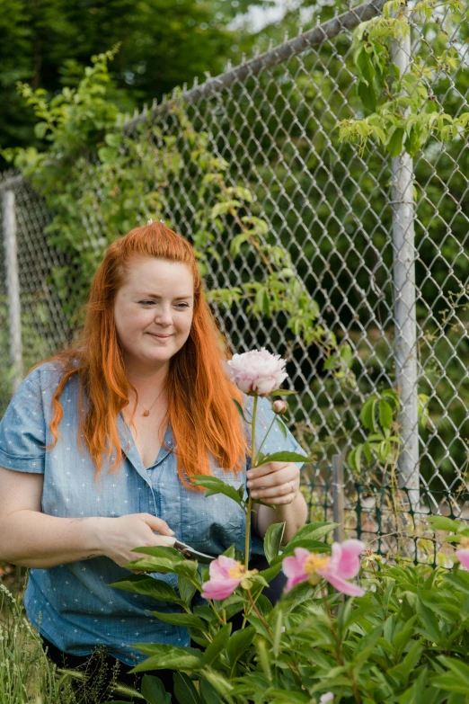 a red - headed woman with red hair smiles at the camera while she is  the flowers