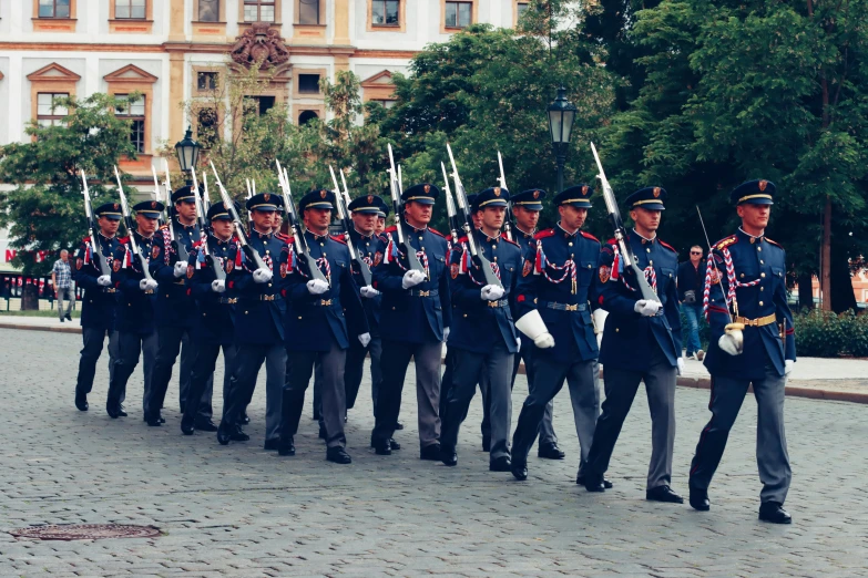 a line of men in blue uniforms walk together on cobblestone street