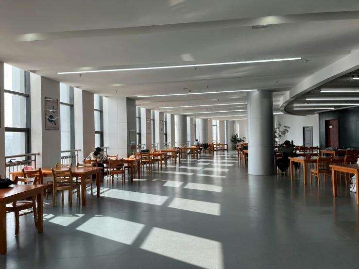 long, open dining room with high windows at one end and large wooden tables and chairs at the other