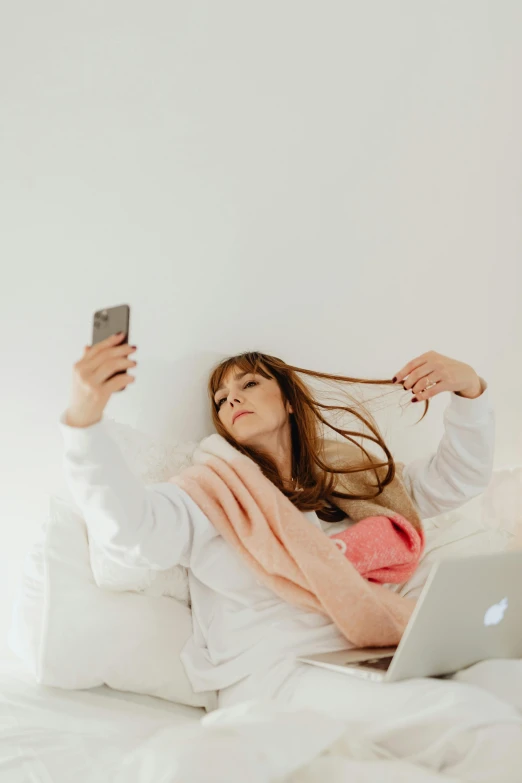 a woman laying in bed holding up her cell phone