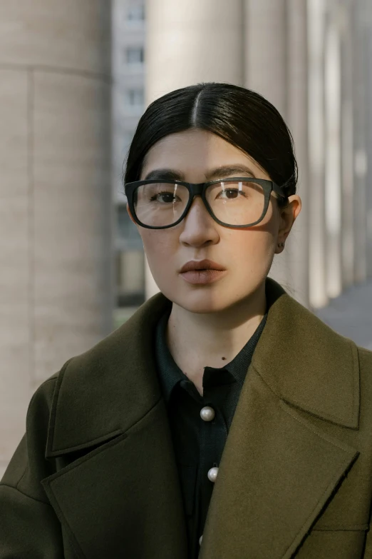 a young woman in glasses standing near a wall