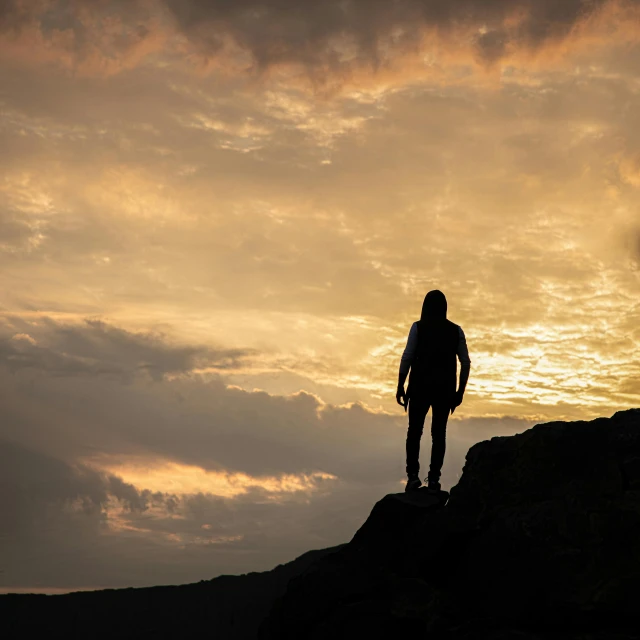 silhouette of person standing on edge of hill with sky in background