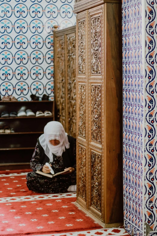 a woman sitting down reading on the floor in front of an elaborate wooden wall