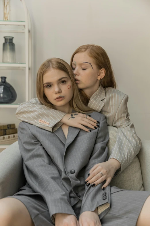 two girls dressed in clothing hugging on a couch