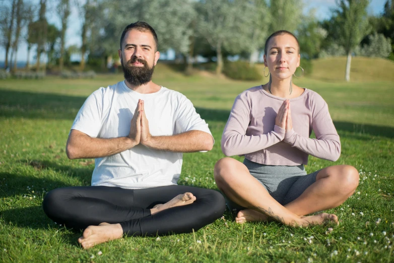 a man and woman sitting in the grass, meditating