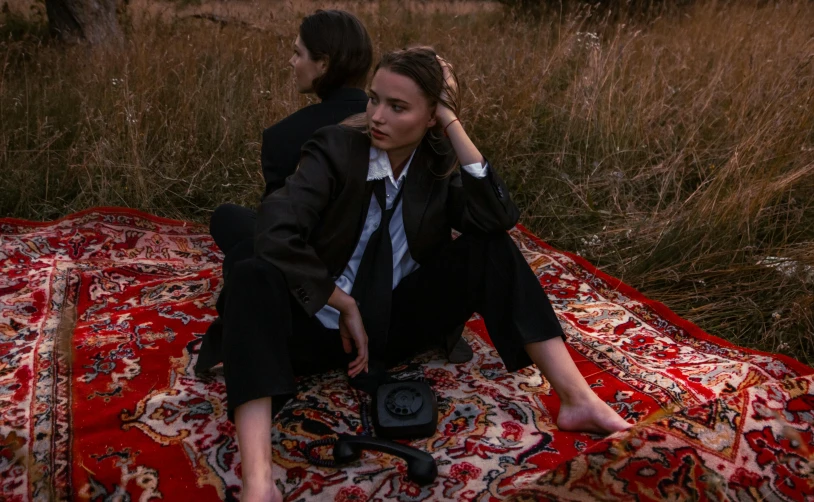 a man and woman sit on top of a carpet in a grassy field