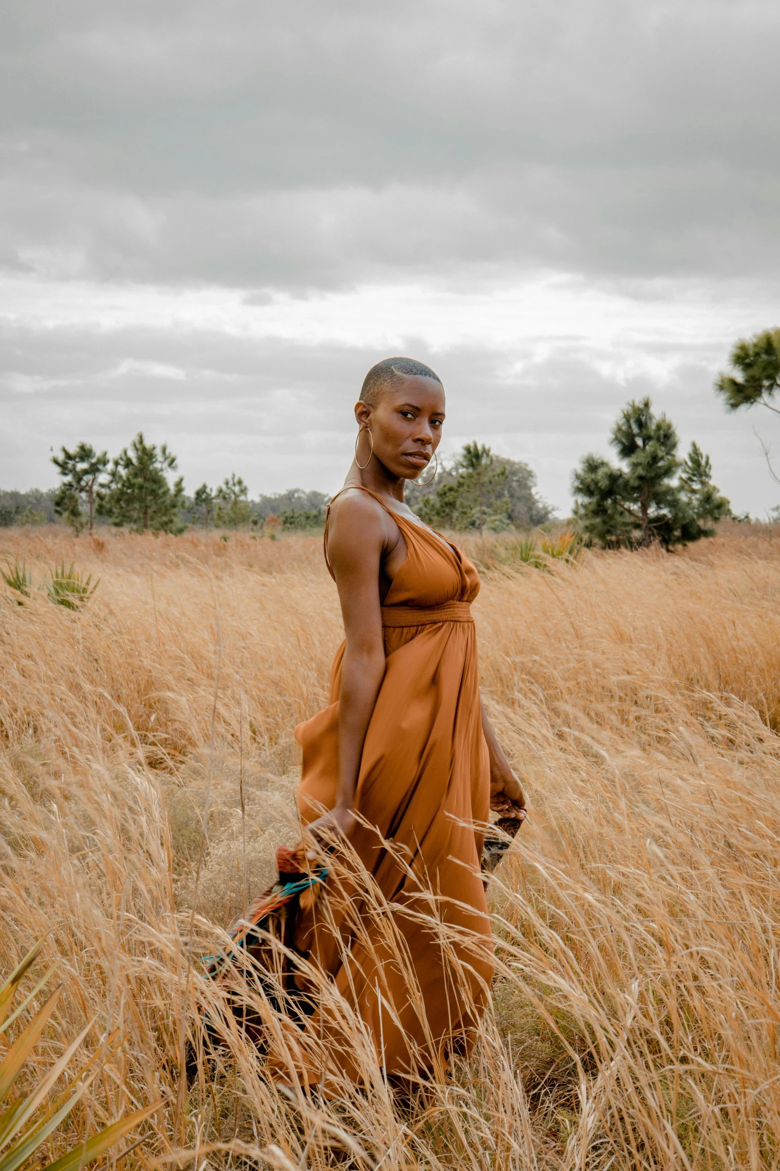 a woman stands in tall grass with her hands in the back pocket