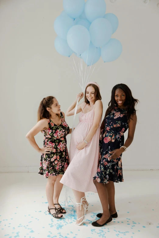 three women smiling while standing together with blue balloons