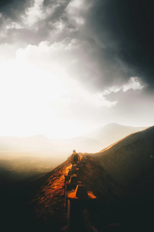 a person sitting on the side of a hill under a cloudy sky