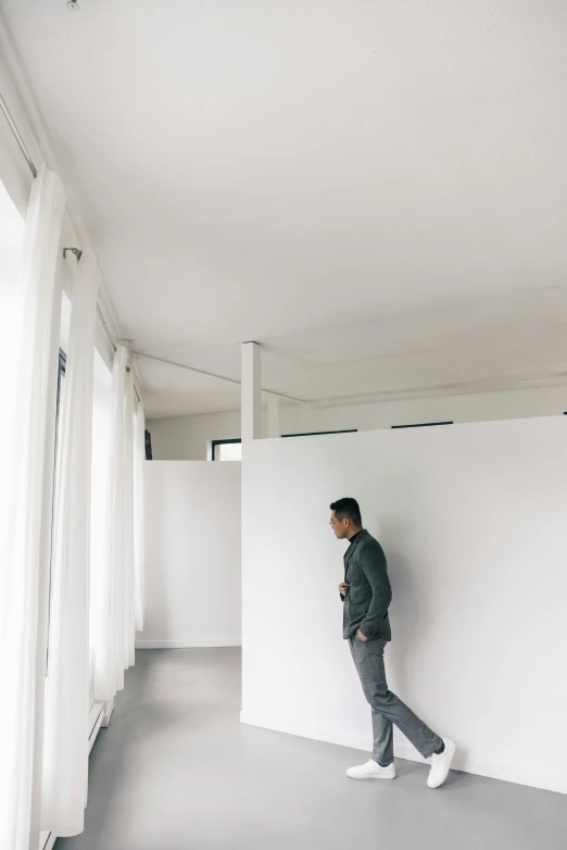 man in black jacket leaning against a white wall