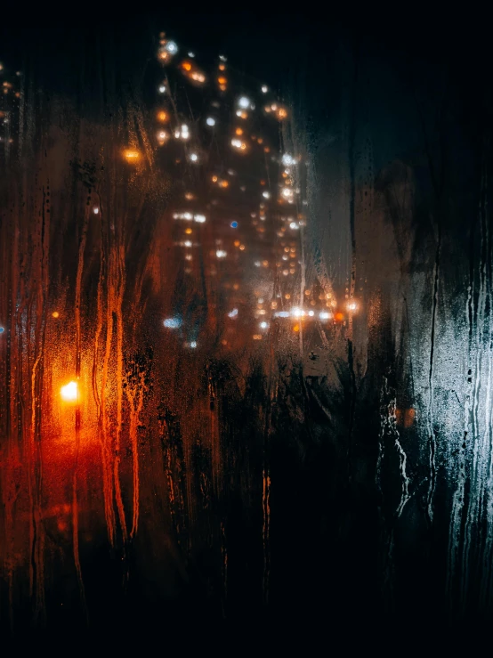 rain is pouring on a window with a city in the distance