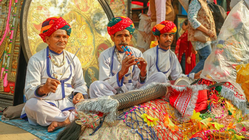 some men with indian headdress and bright colors sit on a cloth