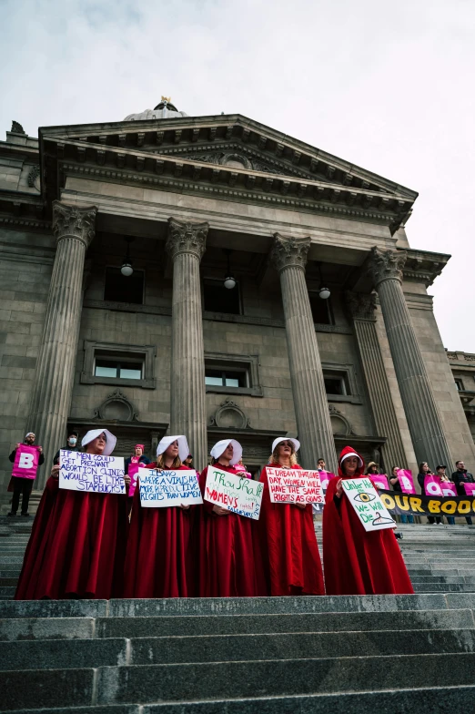 women hold signs at the top of stairs in front of large building