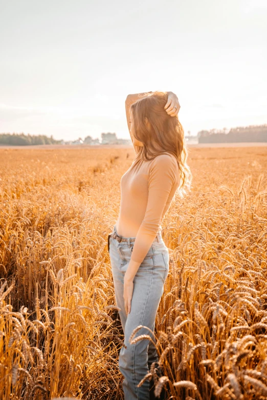 a woman standing in a field of wheat in the sunlight