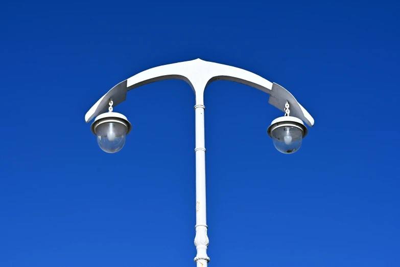 the top of an all white lamp post against a blue sky