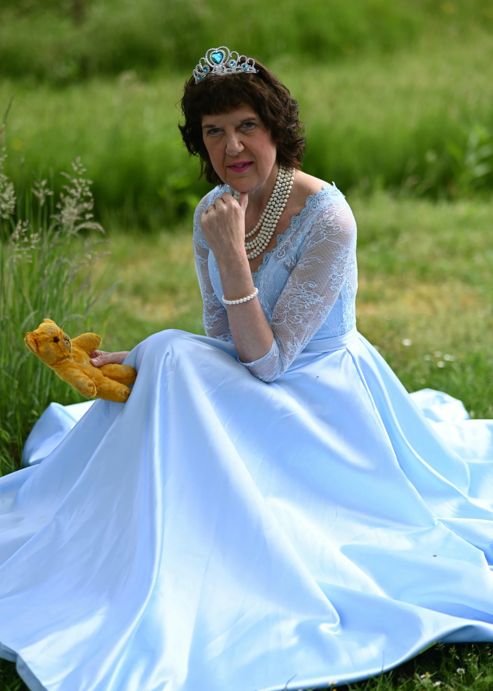 a woman wearing a gown and a crown sitting on the ground