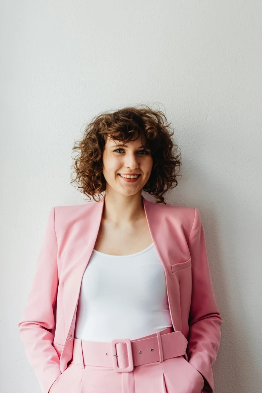 woman in pink suit posing by a white wall