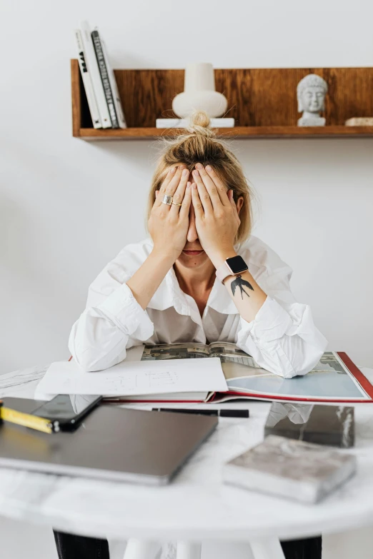 a woman sitting at a desk is covering her face