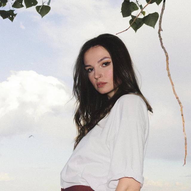 a woman in a white top and red pants standing under a tree