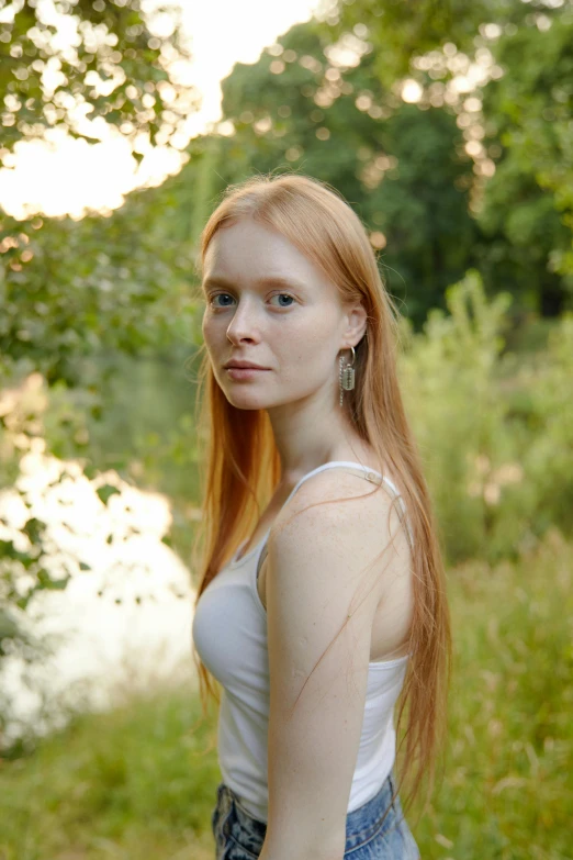 a young redhead woman standing near water and greenery