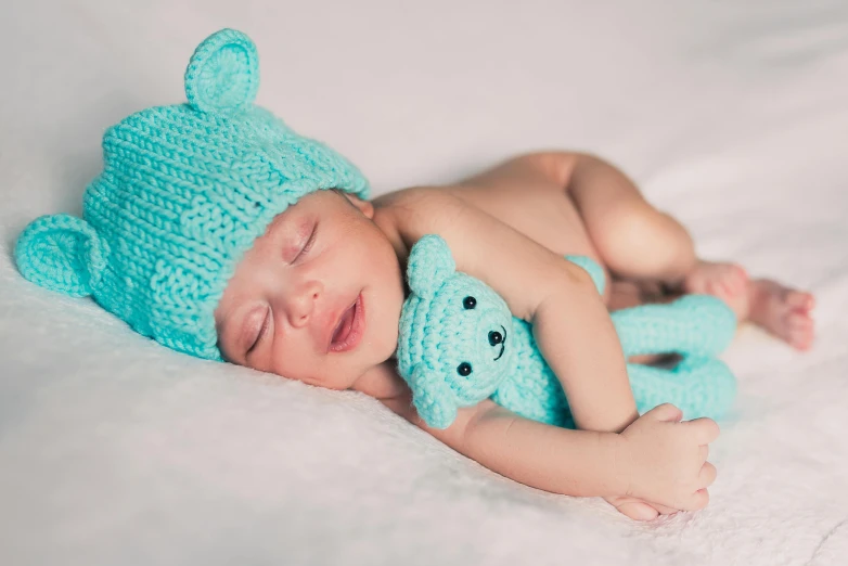 a baby sleeping on the bed with his teddy bear