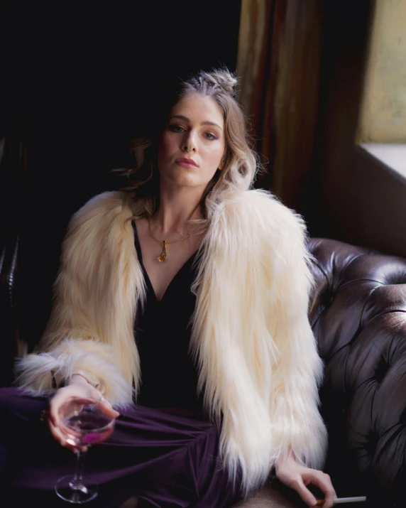 the woman is wearing a fur coat, and a wine glass