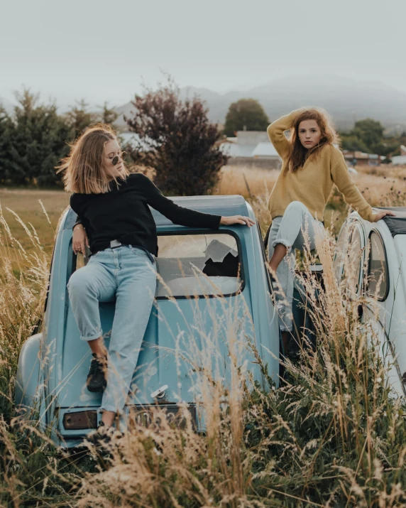 two women sitting on top of the hood of a blue pick up truck