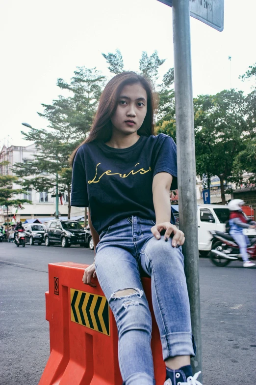 a woman sitting on a street sign near a busy street