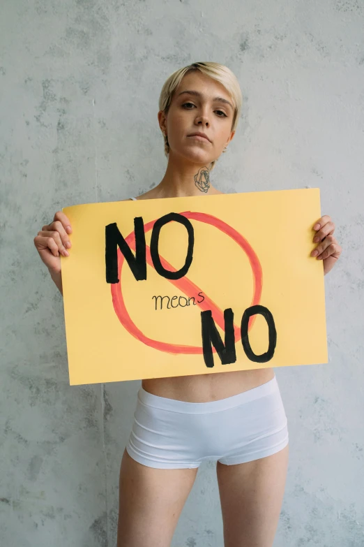 a person standing in shorts holding up a sign that reads no more