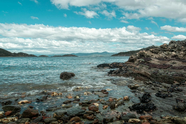 some rocks are by the water and there is a very large rock out in the water