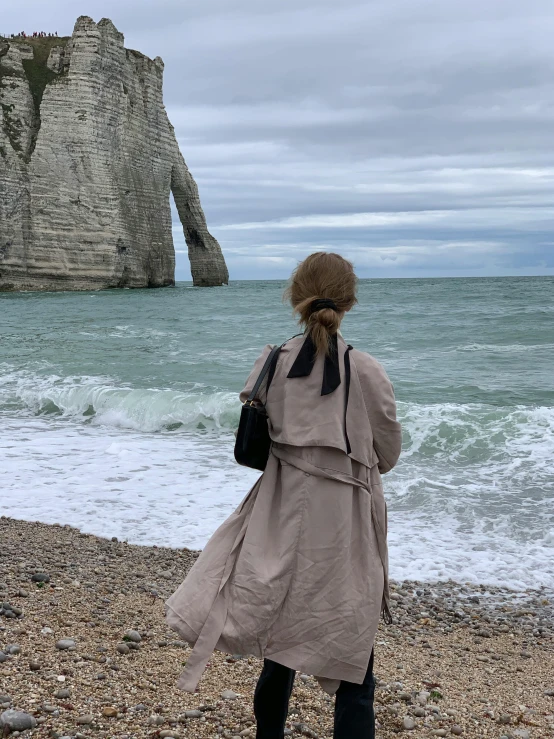 a woman walking on the beach in a brown coat