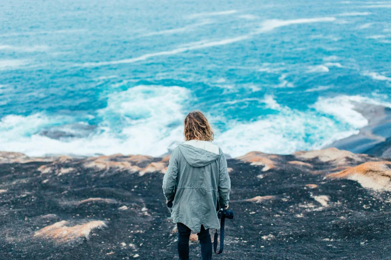 a woman standing on the side of a cliff overlooking the ocean