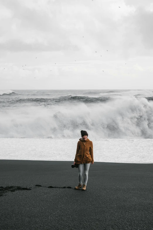 a woman standing on the side of a beach looking at a wave