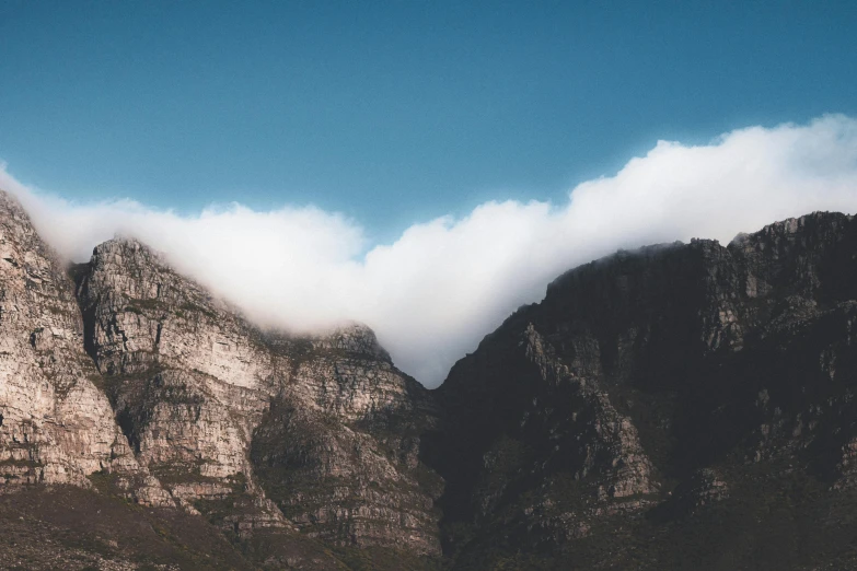 some clouds floating around mountains with a sailboat in the foreground