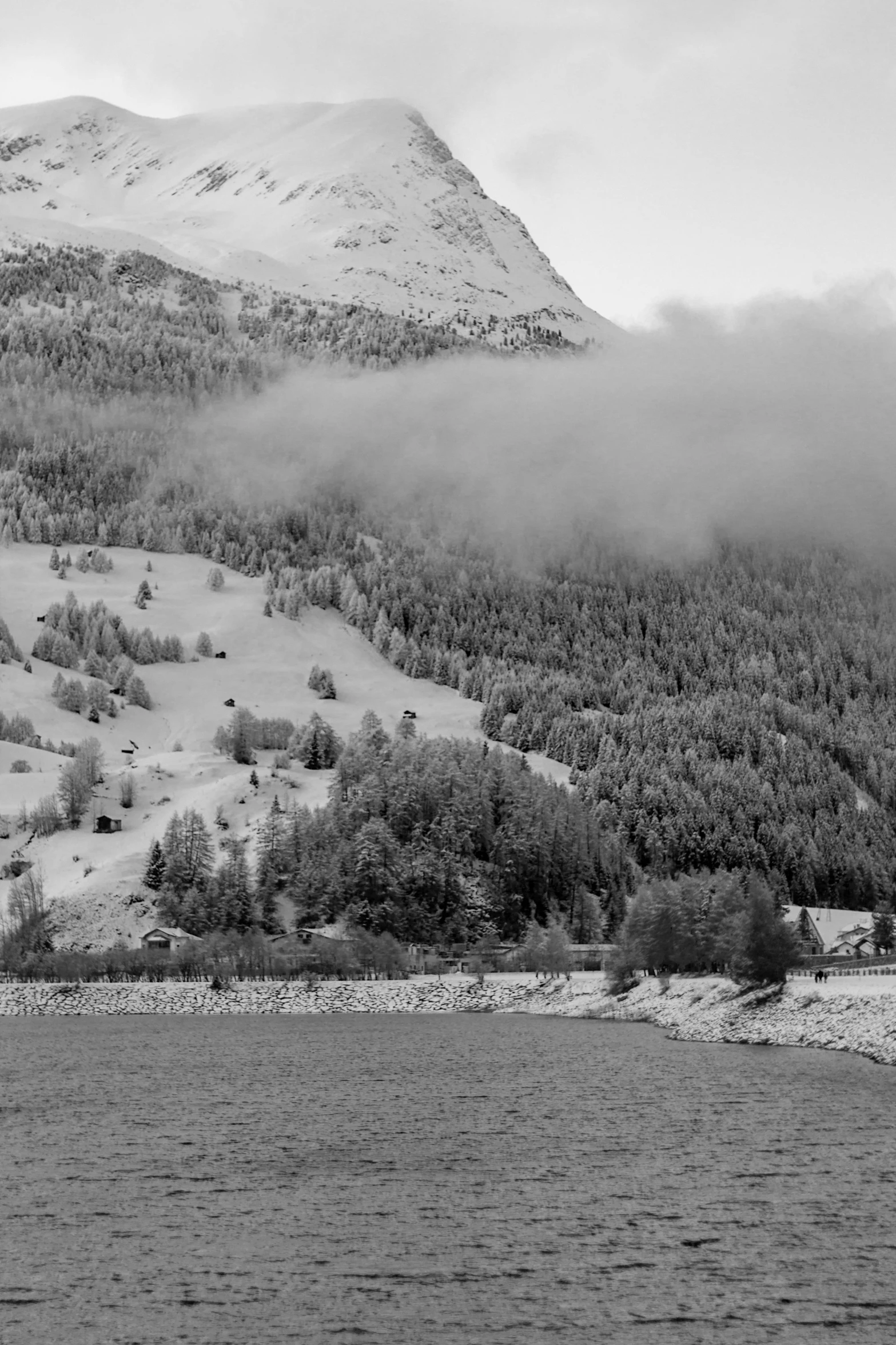 snow capped mountains covered in fog by water