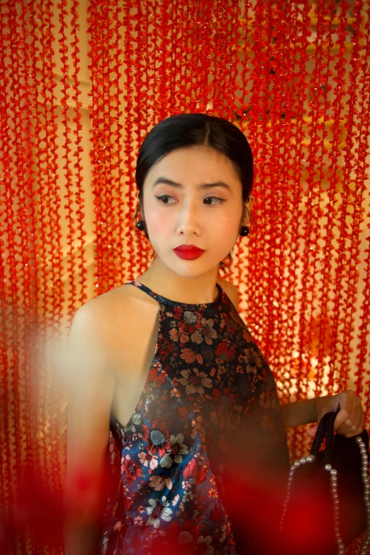 young woman standing in front of red wall with pearls