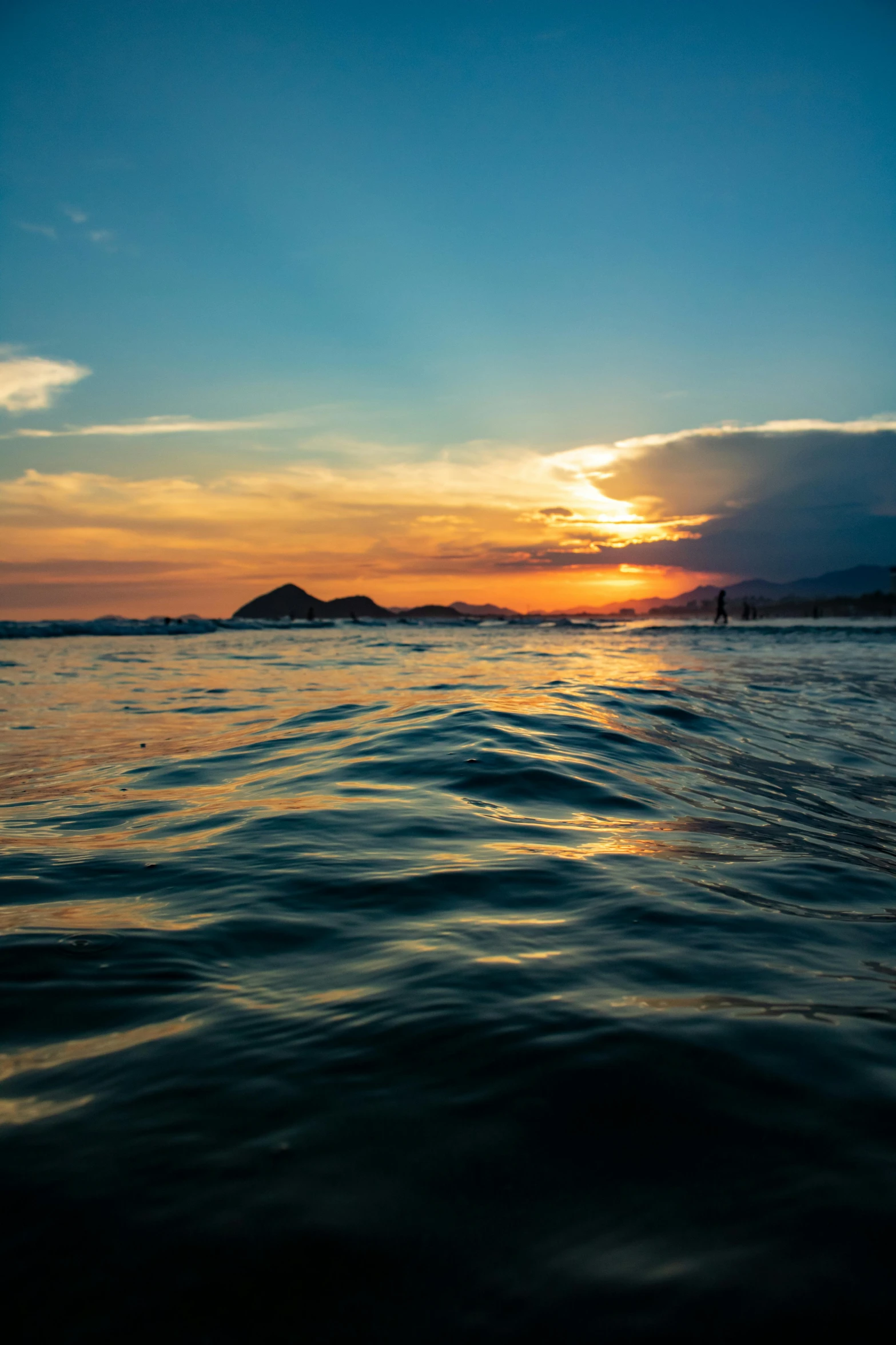 a sunset is over the water with two people standing on a hill