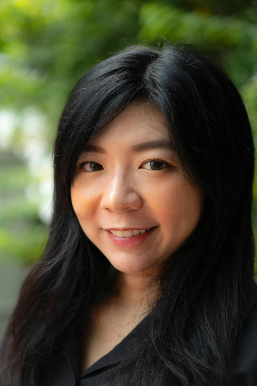 an asian woman smiling with trees in the background