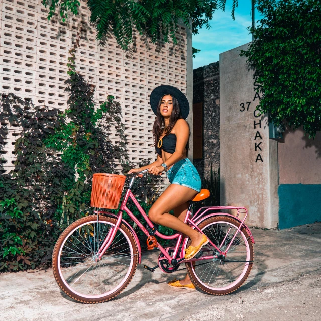 woman riding pink bicycle on dirt ground near plant and white wall