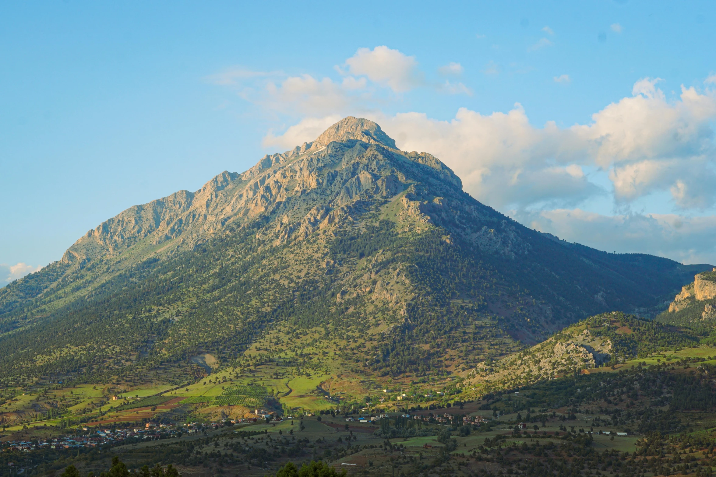 a mountain with mountains in the background, and trees on both sides