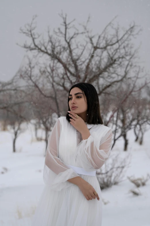 a young woman in a white dress standing outdoors in the snow