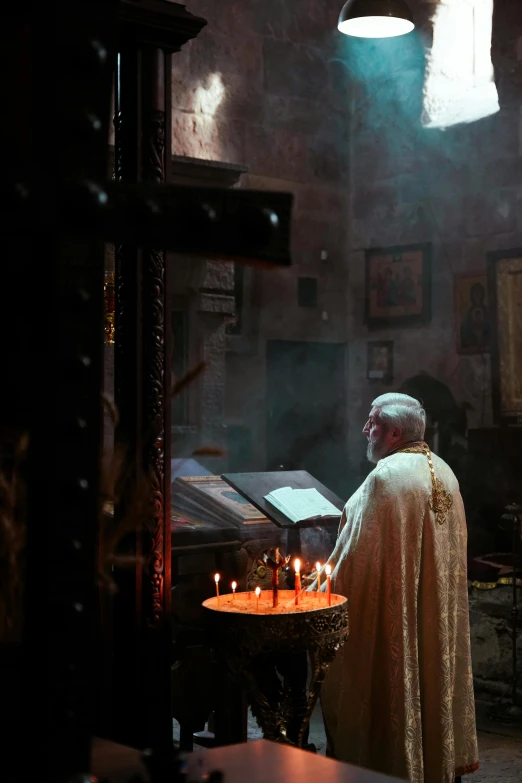 a priest standing at a table that has a lit candle in front of it