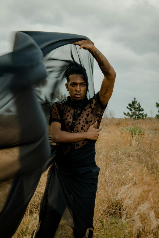 a man holds on to his long black shirt in the middle of a field